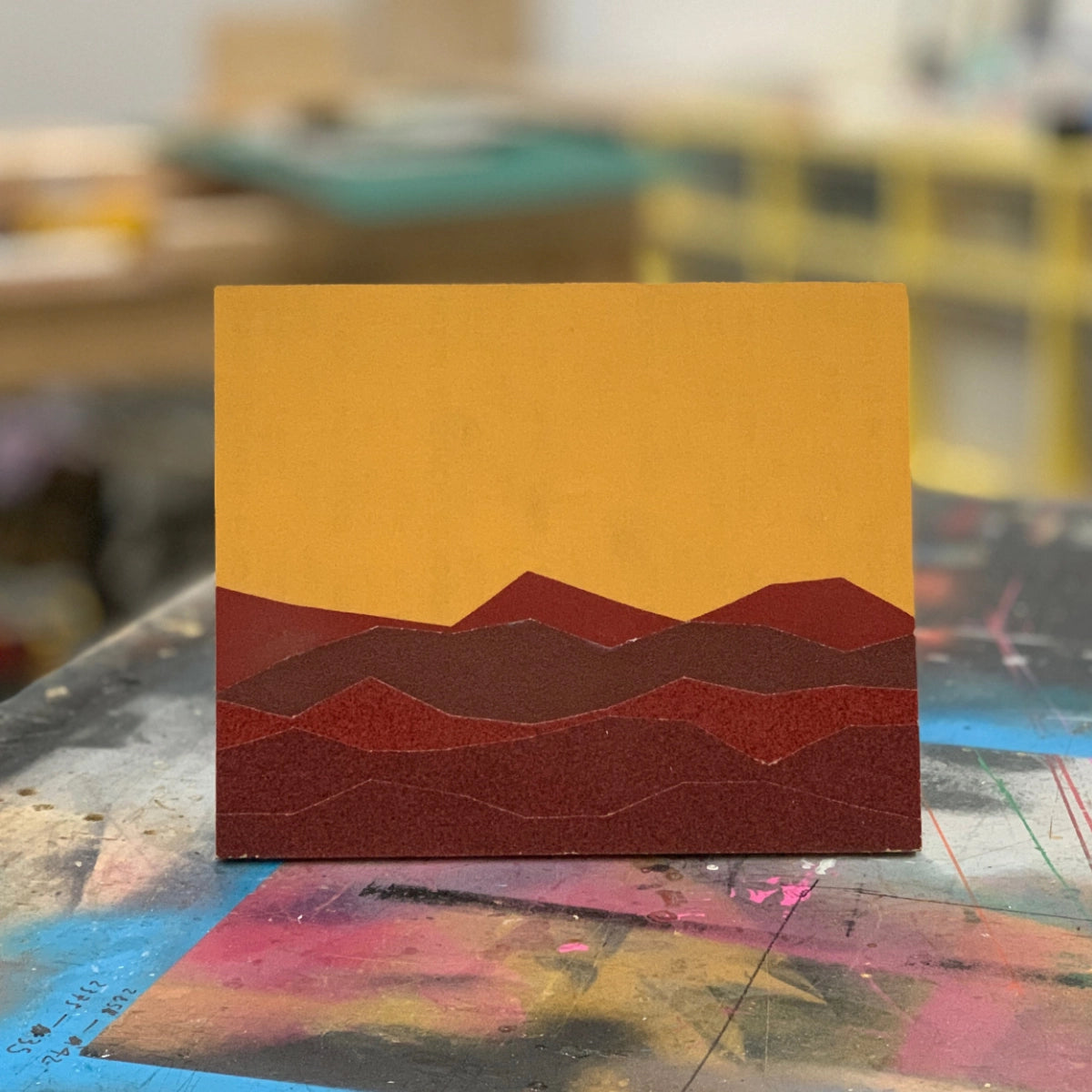 Minimal landscape artwork composed of layered geometric shapes and warm colours.